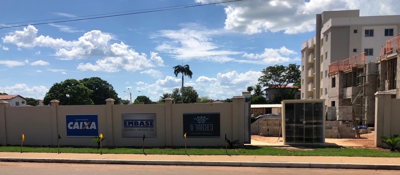 Muro de obra com placas da Caixa como agente financeiro, da EMBASE como construtora e do Condomínio Residencial W Marchesi